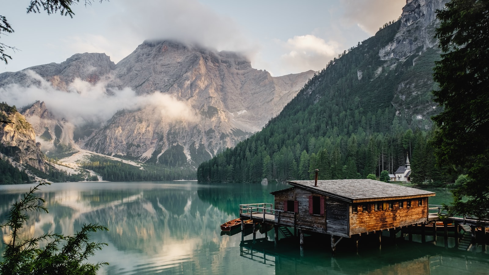 A calm alpine lake reflecting mountains under a clear sky on a hiking trail